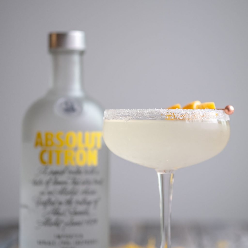 lemon drop garnished with a twist of lemon and a bottle of absolut citron