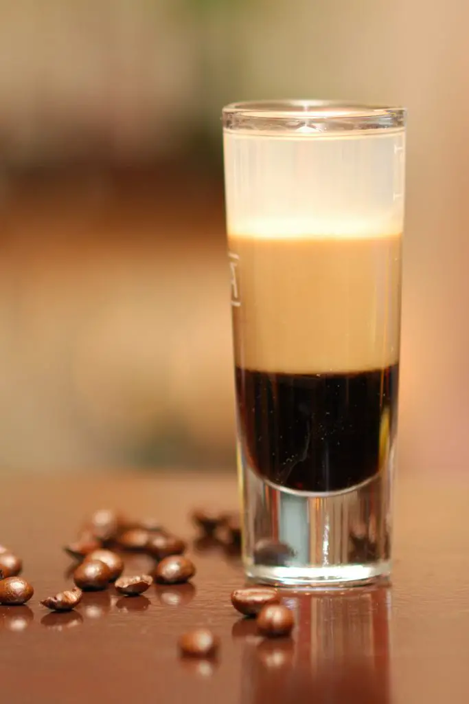 B52 coffee liqueur, baileys and grand marnier layered liqueur in a shot glass with some coffee beans spread on the table. 