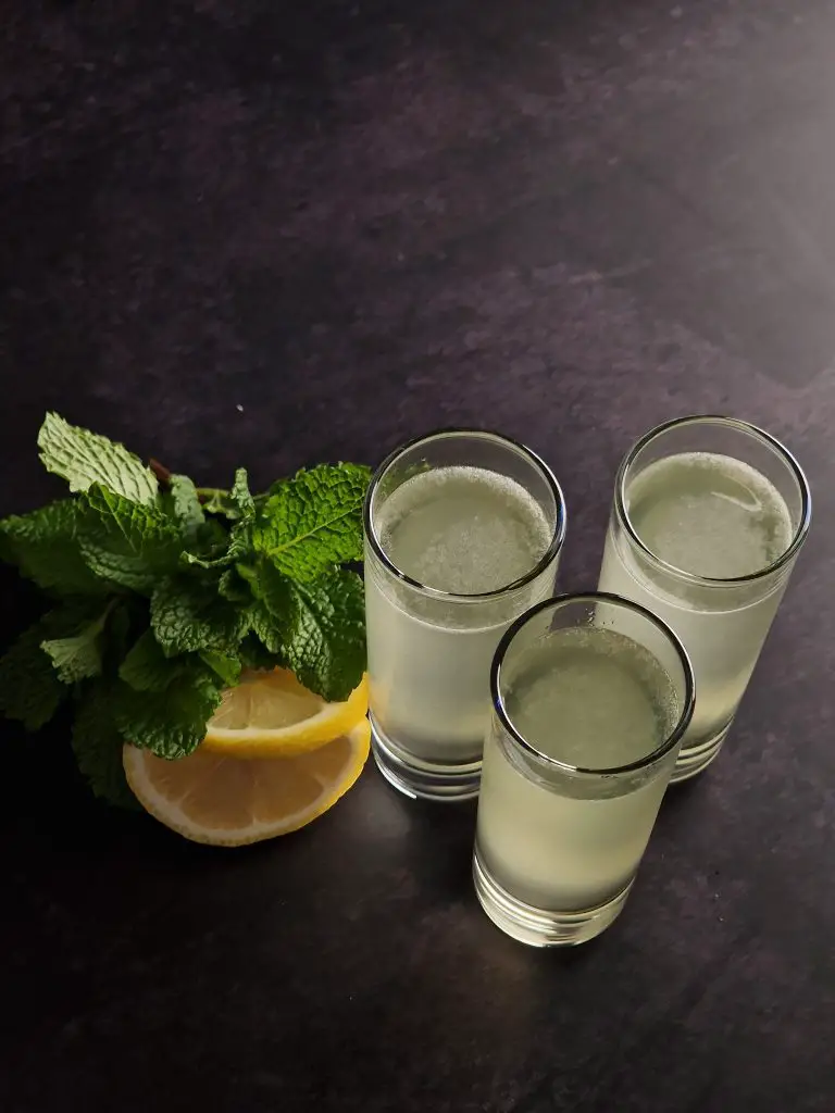 limoncello margarita cocktail shot in 3 slim cocktail glasses on a dark background with lemon and fresh mint leaves high angle view