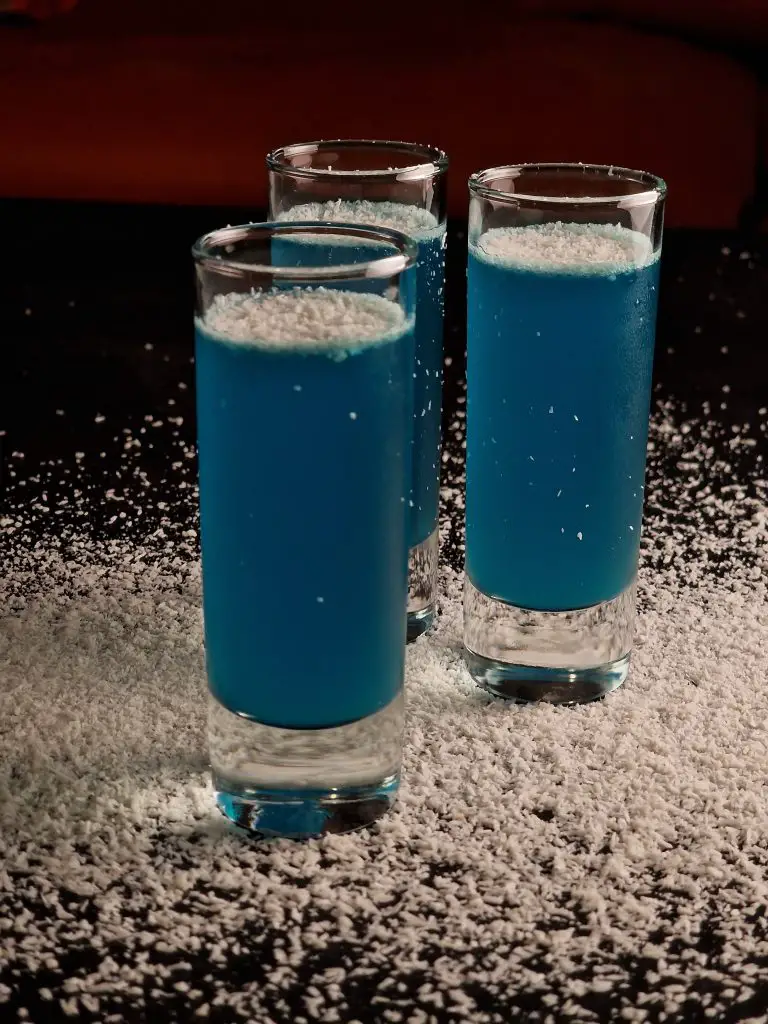 3 shot glasses filled with blue coconut cocktail shots, made with rum, blue curacao and fresh lemon juice.