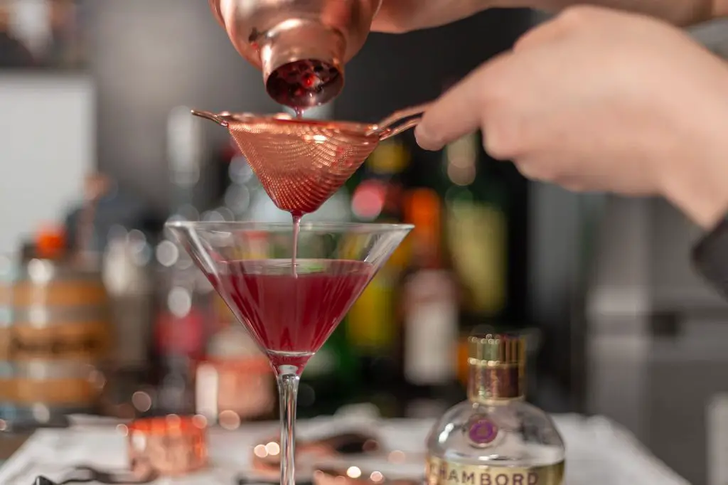 pouring drink in cocktail glass using a sieve