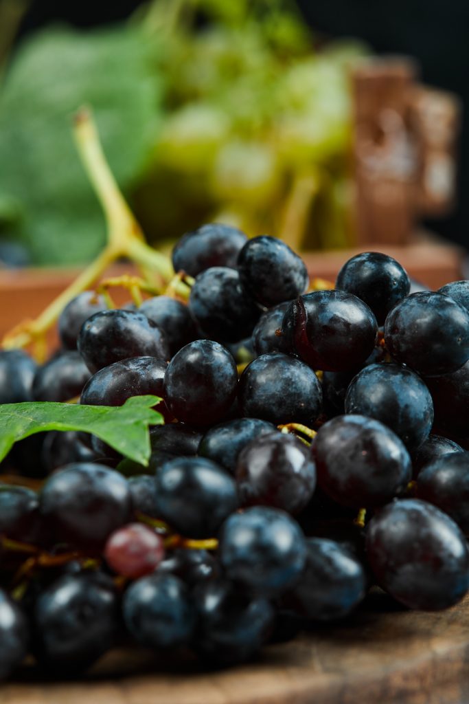 A cluster of black grapes on wooden plate, close up.