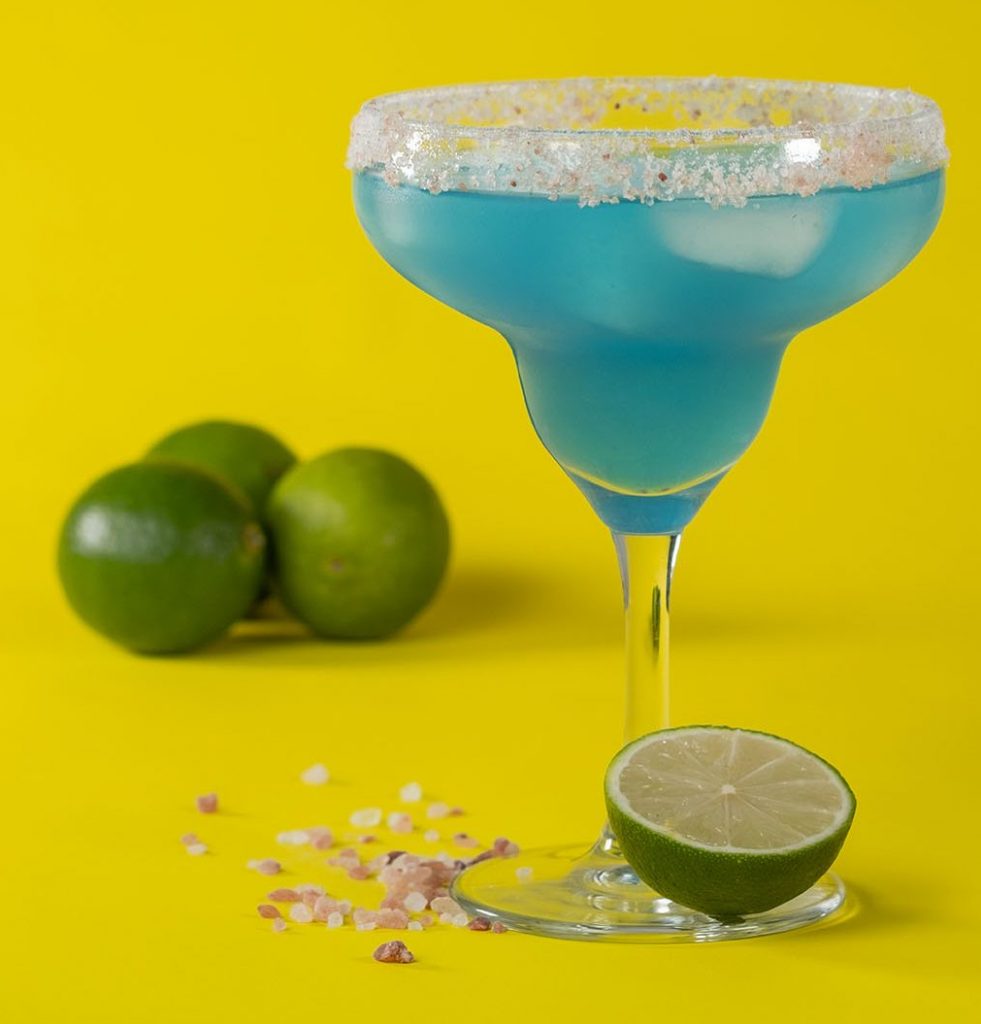 Blue margarita on yellow background with limes