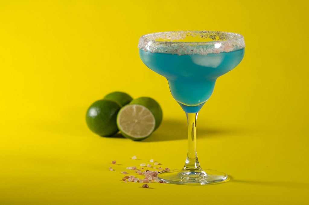 blue margarita with limes and himalayan salt on yellow background
