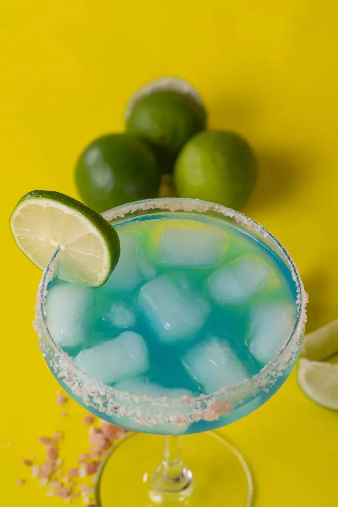 blue margarita with limes and salt garnished with a slice of lime and glass full of ice