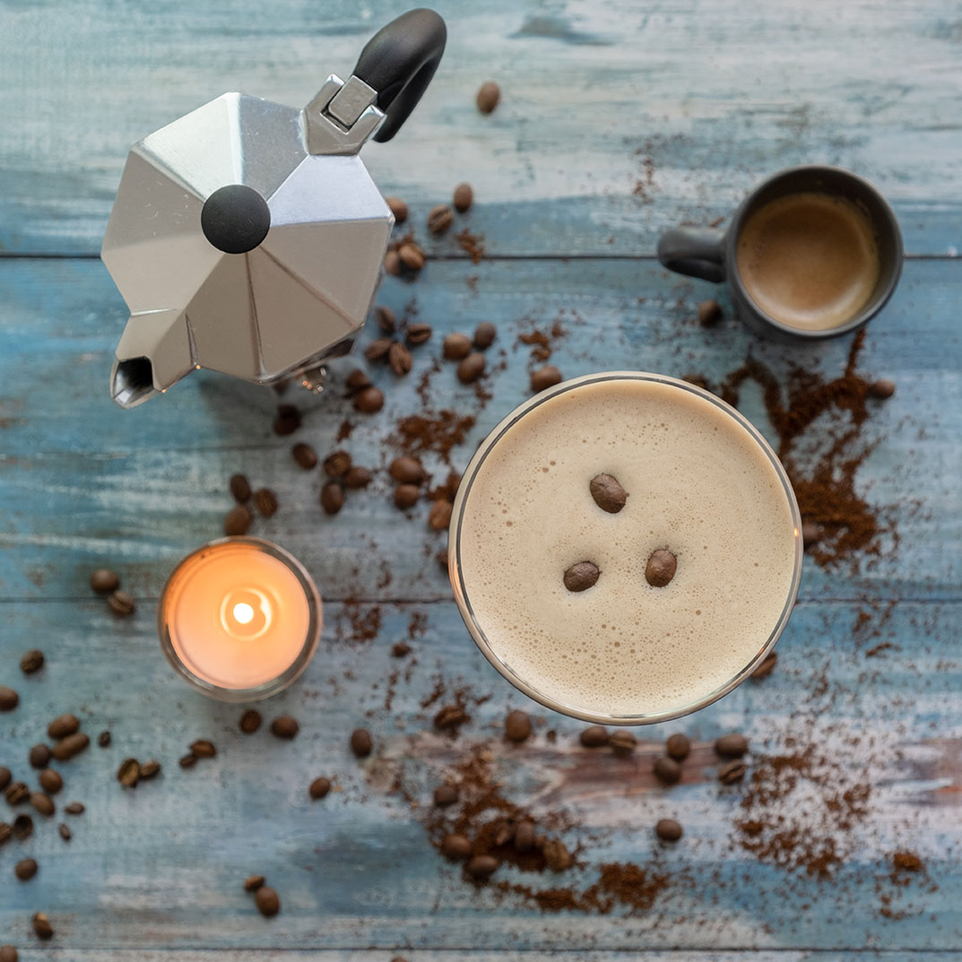 Espresso martini with mocha pot and lighting candle on a wooden table spread coffee beans