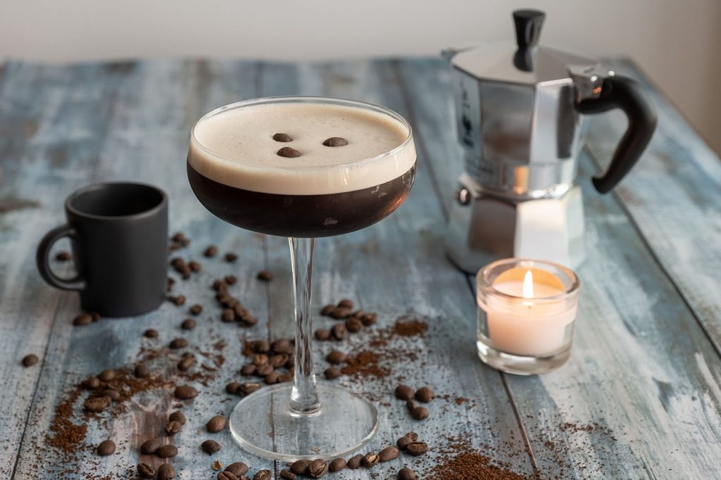 espresso martini in a coupe glass with mocha pot, coffee and candle, coffee spread on the wooden table