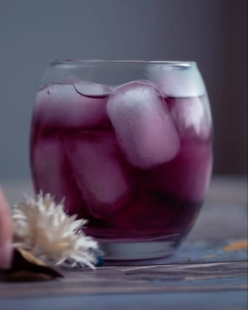 purple cocktail in a glass filled with ice