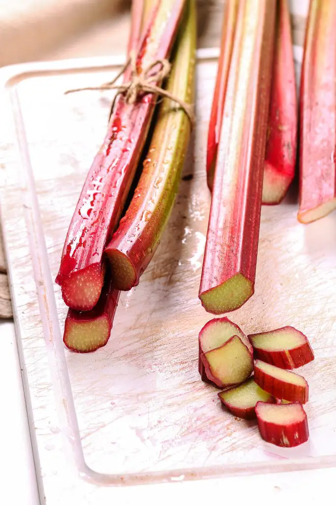 Rhubarb sticks on a cutting board, there are some sliced pieces.