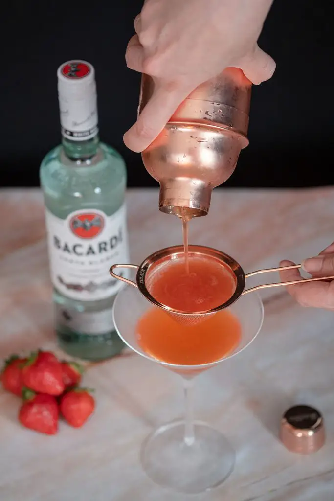 A hand pouring strawberry daiquiri from a shaker in a chilled martini glass.