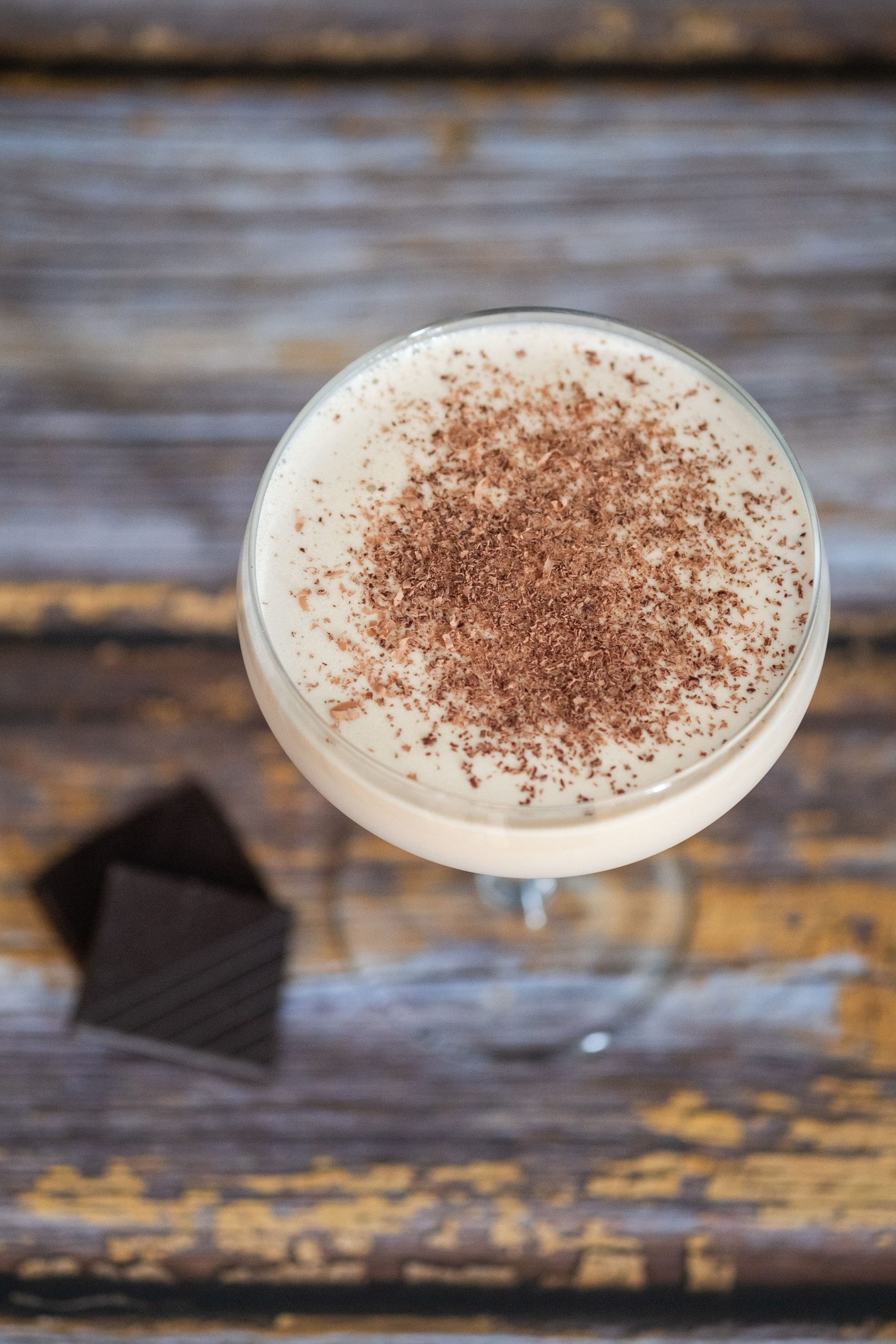 mudslide cocktail garnished with chocolate shreds on a wooden table and 2 pieces of dark chocolate next to the glass