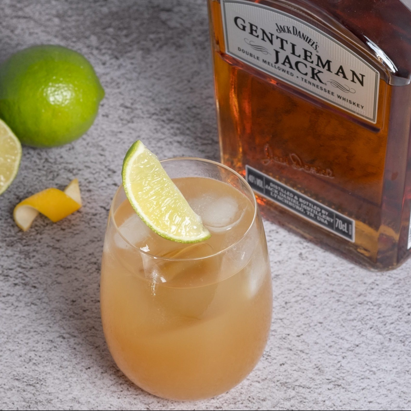 A glass of maple whiskey sour cocktail, a bottle of whiskey is seen on the back