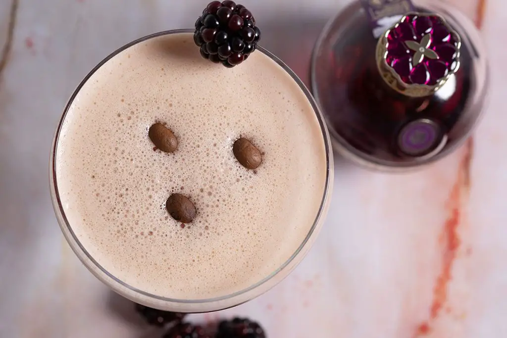 top view of a raspberry espresso martini cocktail on a pink marble glass with a chambord bottle next to it. 