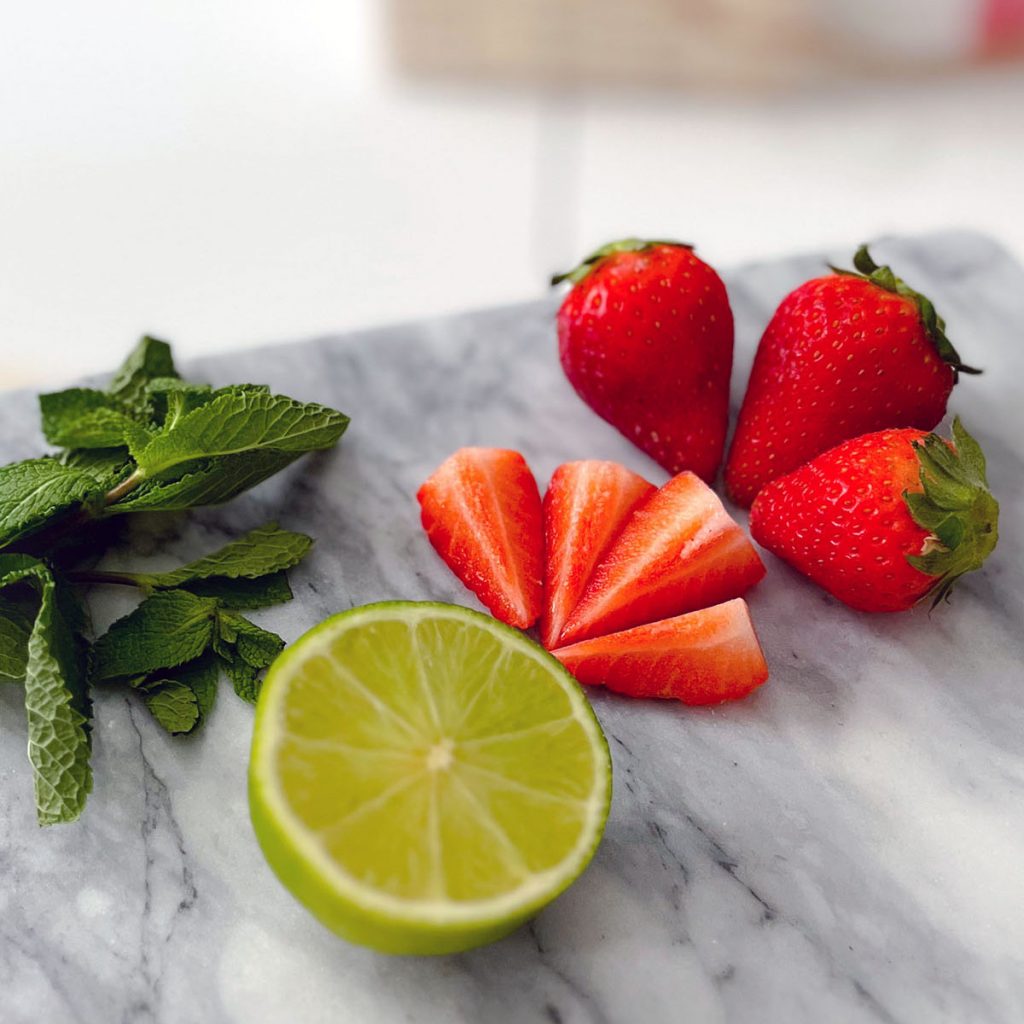 A half lime, fresh mint leaves and some strawberries on a marble background.