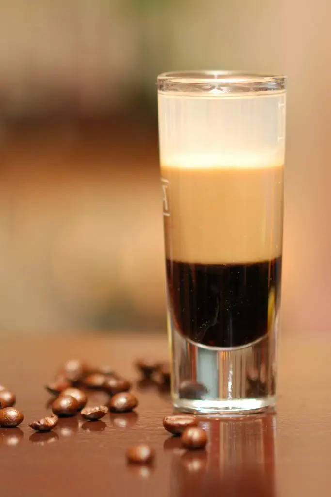 B52 coffee liqueur, baileys and grand marnier layered liqueur in a shot glass with some coffee beans spread on the table.