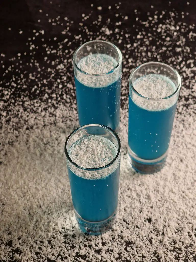 3 slim cocktail glasses with blue coconut cocktail high angle view with shredded coconut spreaded all around