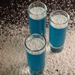 3 slim cocktail glasses with blue coconut cocktail high angle view with shredded coconut spreaded all around