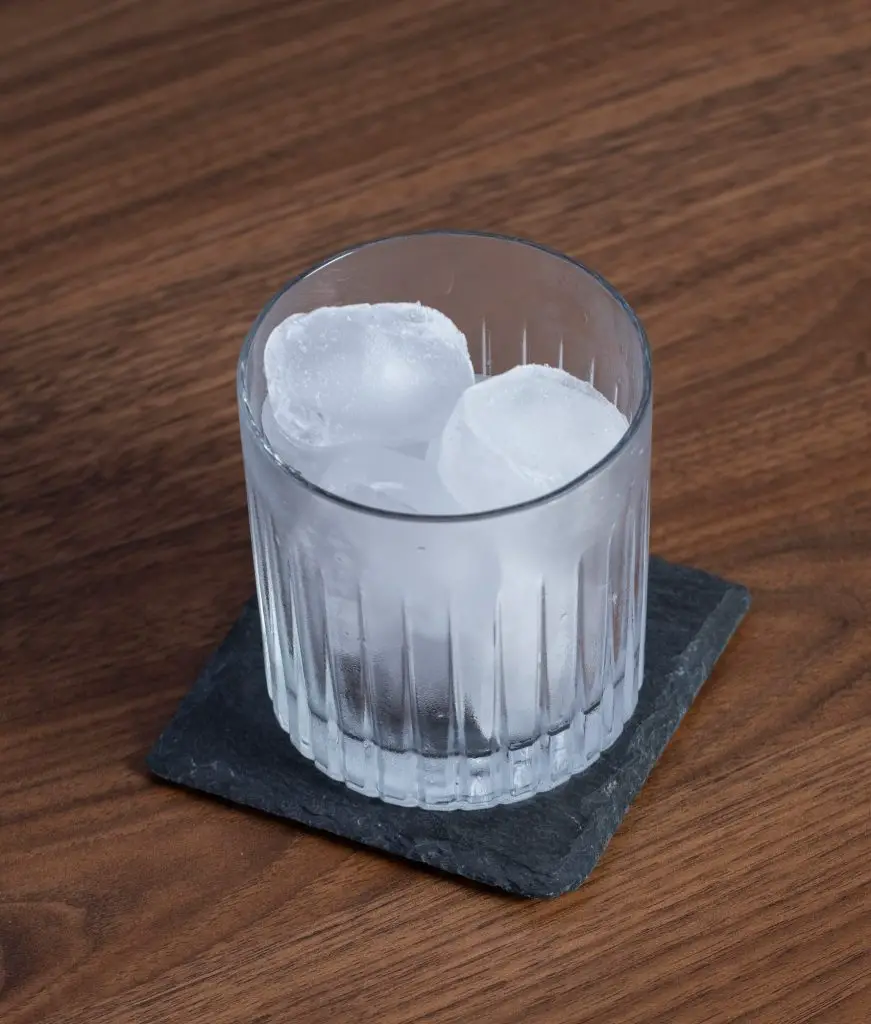 An old fashioned glass filled with ice, on a black rock coaster on a wooden table, high angle shoot.