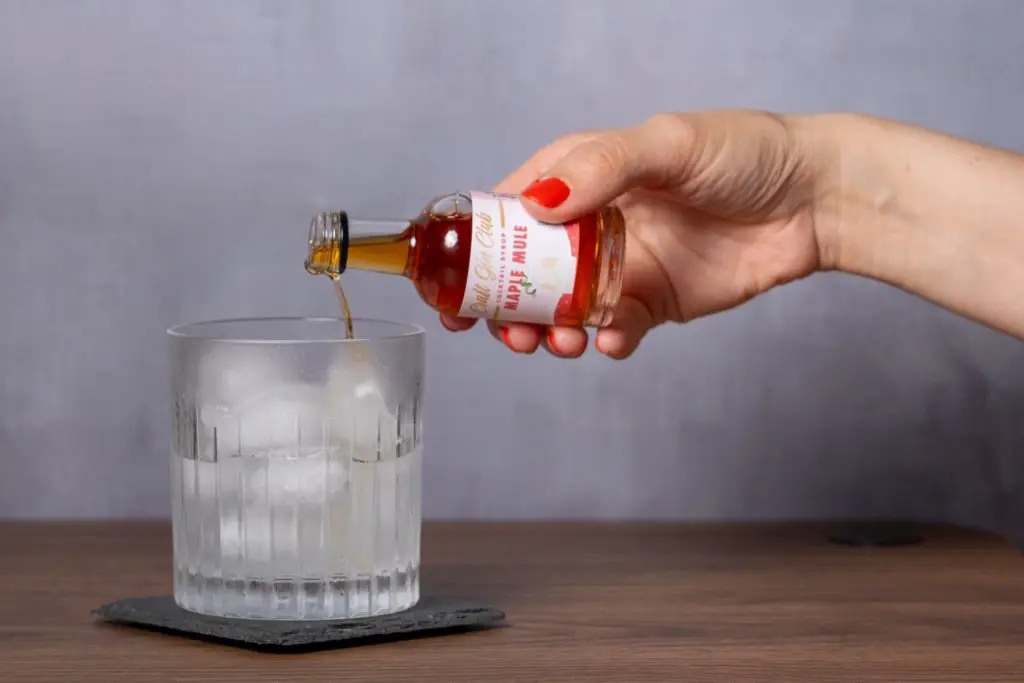A woman's hand pouring maple mule syrup into the cocktail glass.