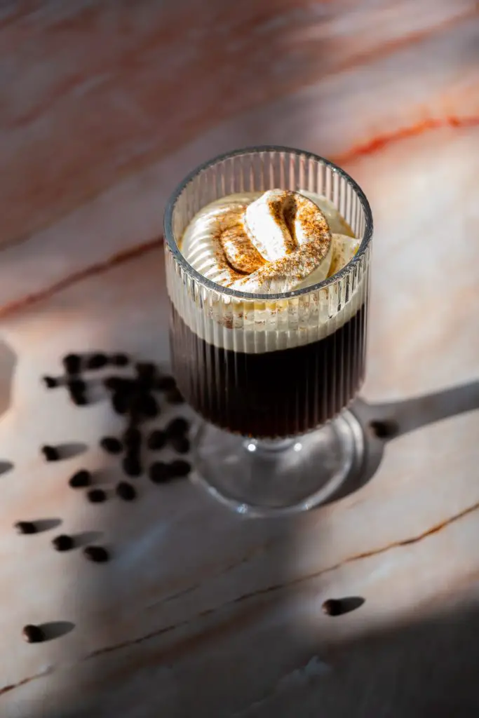 irish coffee cocktail on a pink marble table with some coffee beans spread on the table. high angle view.